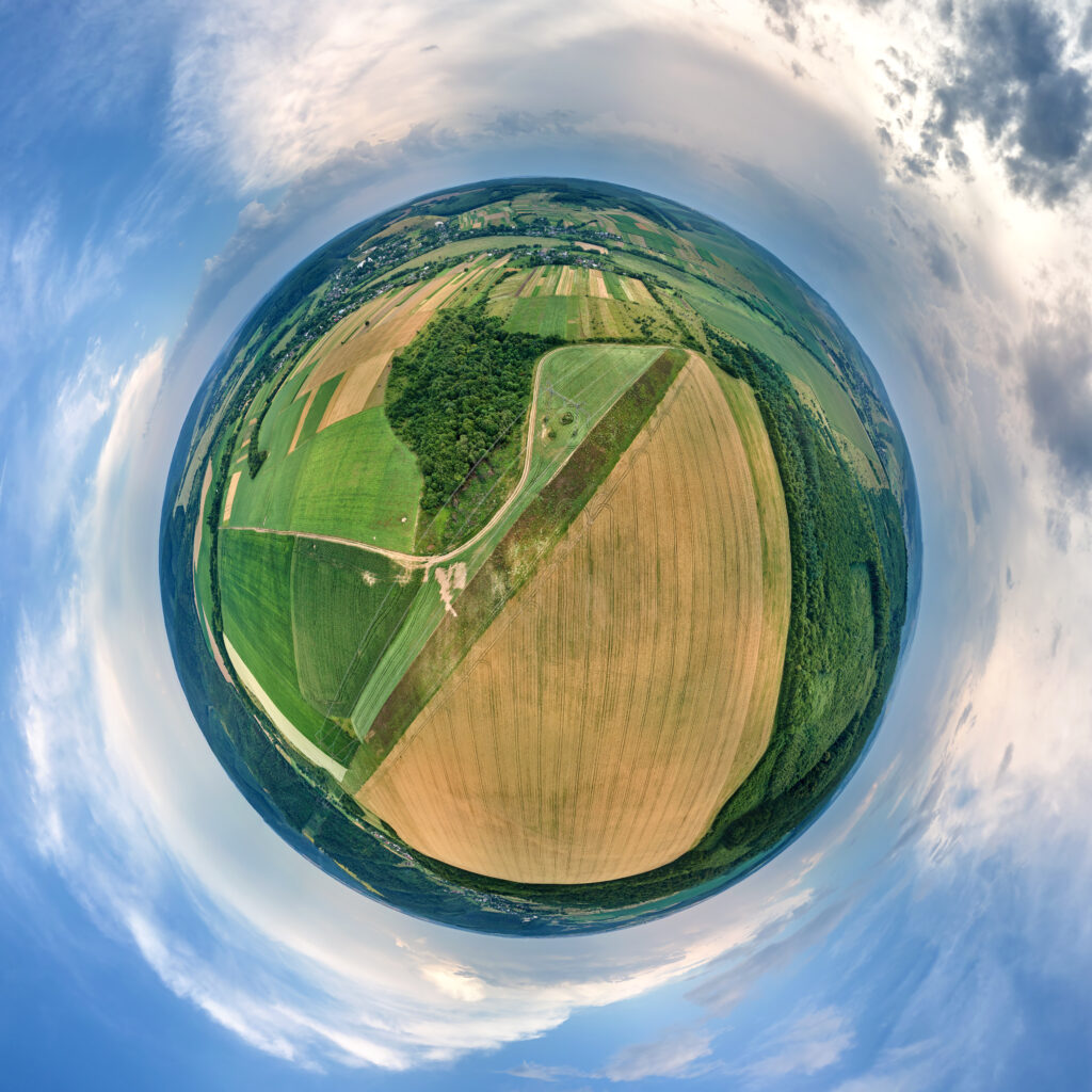 Aerial view from high altitude of little planet earth with yellow cultivated agricultural fields with ripe wheat and green woods on bright summer day
