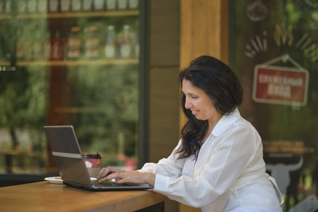smiling mature businesswoman drinking coffee while working in cafe
